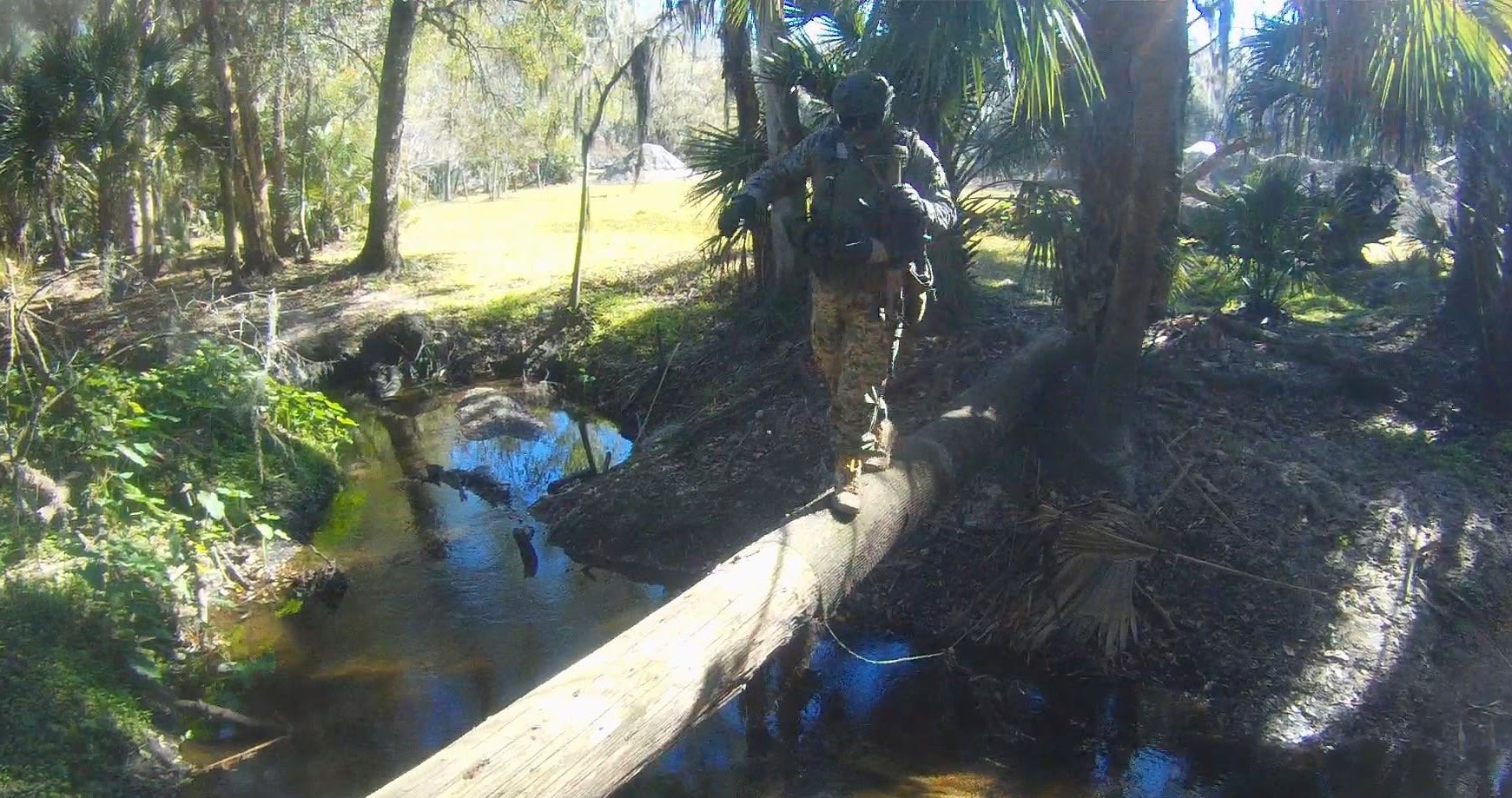Player in flecktarn camo crossing a stream on a fallen log at Amerika
