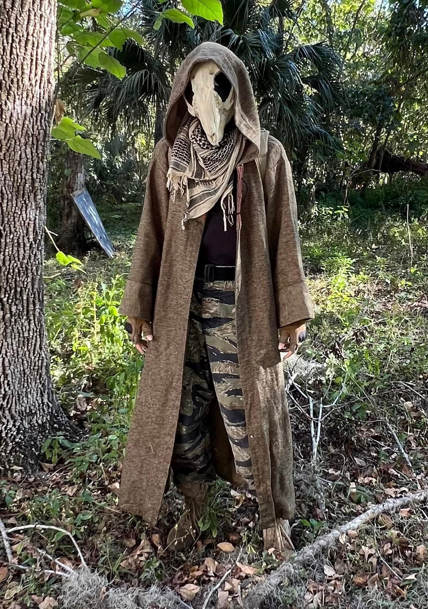 Hooded player with bird skull mask in forest