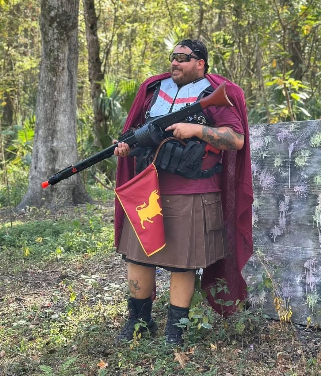 Roman-style player in maroon cape with airsoft rifle